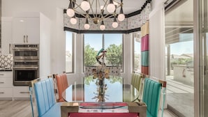 Une cuisine moderne avec une table à manger en verre, des chaises colorées et un lustre central.