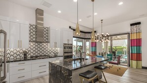 Une cuisine moderne avec des meubles blancs, un îlot en marbre, des appareils en acier inoxydable et des luminaires suspendus.