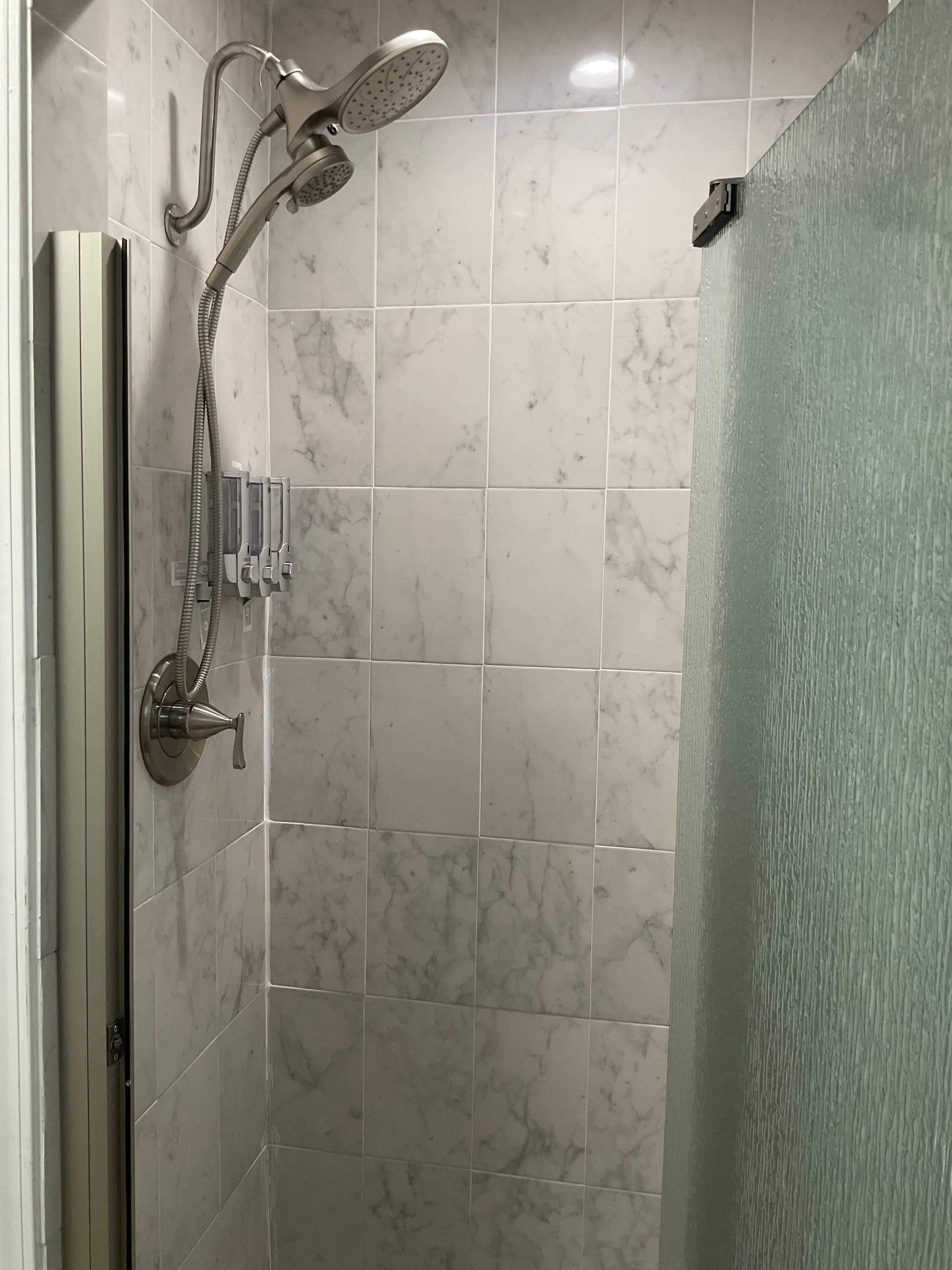 Ducha con cabezal de ducha manual y panel de control en la pared.