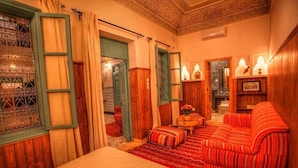 A traditional room with a bed, a sofa, a small table with a vase, and a patterned rug.