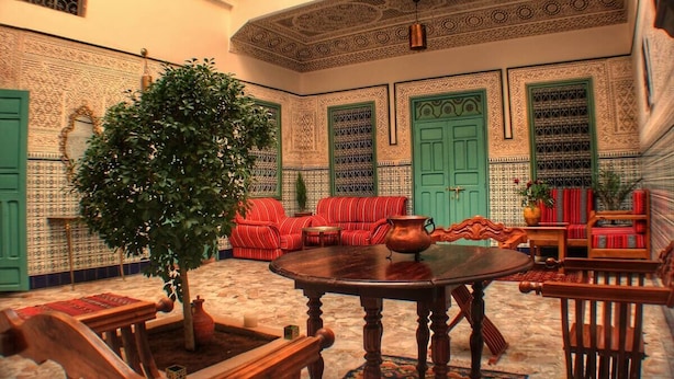 A traditional Moroccan interior with ornate tile walls, green doors, and red striped sofas.