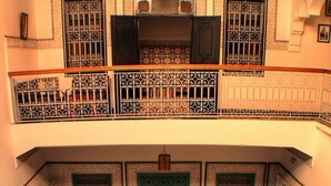A traditional interior with a courtyard, a balcony with ornate railings, and a tiled floor.