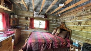 Une chambre rustique, aménagée comme un chalet, avec un lit en bois, une commode en bois, une fenêtre avec des rideaux et une pancarte « Bienvenue » accrochée au mur.