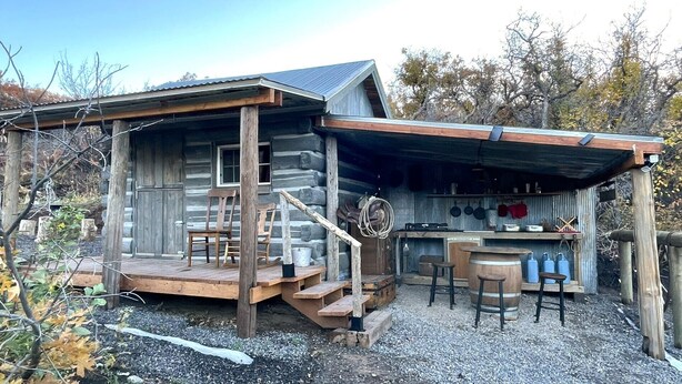 Une cabane rustique dotée d’une terrasse en bois, d’un petit porche et d’un coin bar avec des tabourets.
