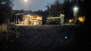 Un bâtiment rustique en bois, doté d’un porche et d’une brouette à l’extérieur.