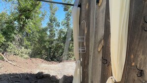 Une structure rustique en bois, dotée d’un robinet métallique, d’un seau noir et d’un tapis à motifs posé sur le sol.