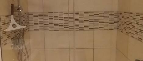 A glass-enclosed shower stall with a tiled floor, a handheld showerhead, and a wall-mounted faucet.