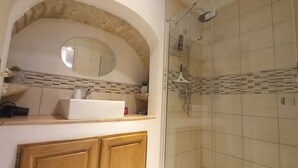 Un baño con lavamanos blanco, un espejo y zona de ducha.