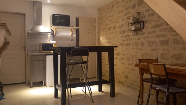 Cocina compacta con microondas, tostadora y estufa. Hay una mesa de comedor con sillas y un taburete pequeño.
