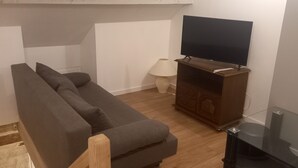 Una sala de estar con un sofá gris, un aparador de madera, un televisor de pantalla plana y una lámpara.