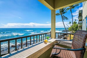 Un balcón con vista al océano, una silla, una mesa con una bebida y una planta tropical.