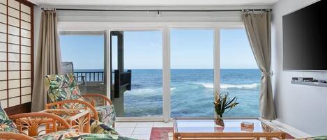 A room with a view of the ocean, a TV, a sofa, and a table with a vase.