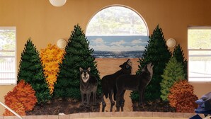 Un mural con lobos y árboles, y una vista a la playa a través de una ventana semicircular.