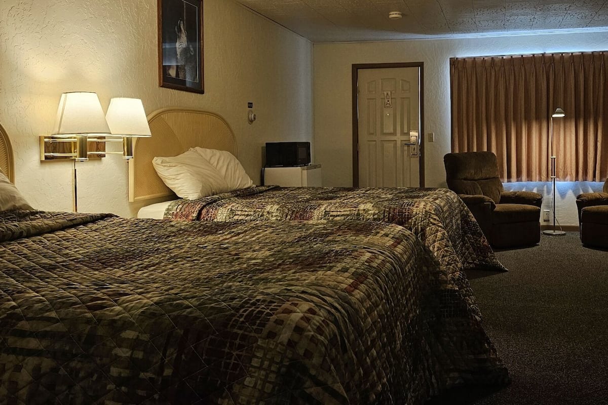 A hotel room with two beds, a desk, a chair, a television, and a door.