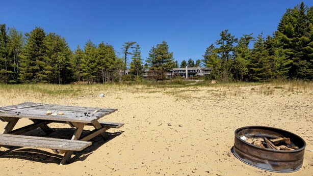 Una playa arenosa con una mesa de picnic de madera y un brasero de metal.