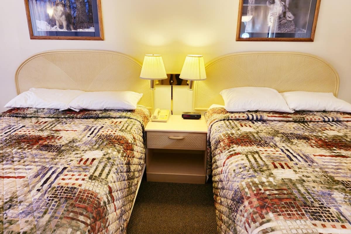 A double room with two beds, each with a patterned quilt, a bedside table with a lamp, and a phone. There are two framed pictures on the wall above the beds.