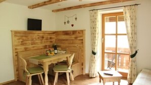 A cozy room with a wooden headboard, a small table with chairs, a window with curtains, and a bed. - Ferienwohnung Untersberg (Berchtesgaden)