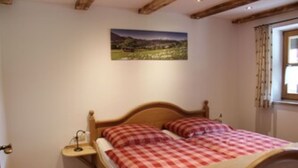 A bedroom with a wooden bed, a nightstand, a painting of a landscape, and a window with curtains. - Ferienwohnung Untersberg (Berchtesgaden)