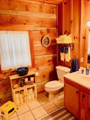 A wooden cabin bathroom with a toilet, sink, and a small shelf with toiletries.