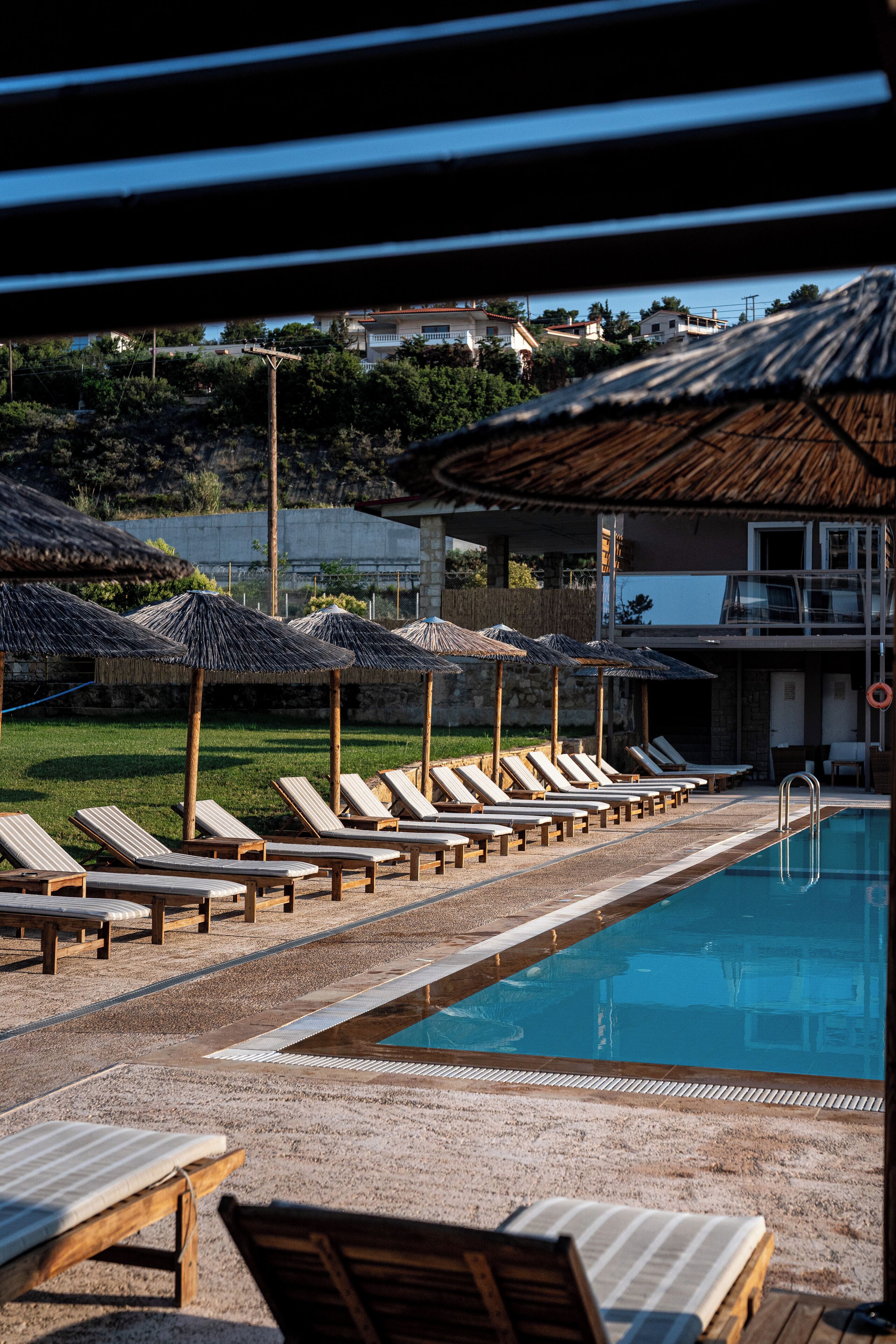 Ein Poolbereich mit Liegestühlen und Sonnenschirmen, ein klares Schwimmbecken und eine Blick auf Gebäude im Hintergrund.
