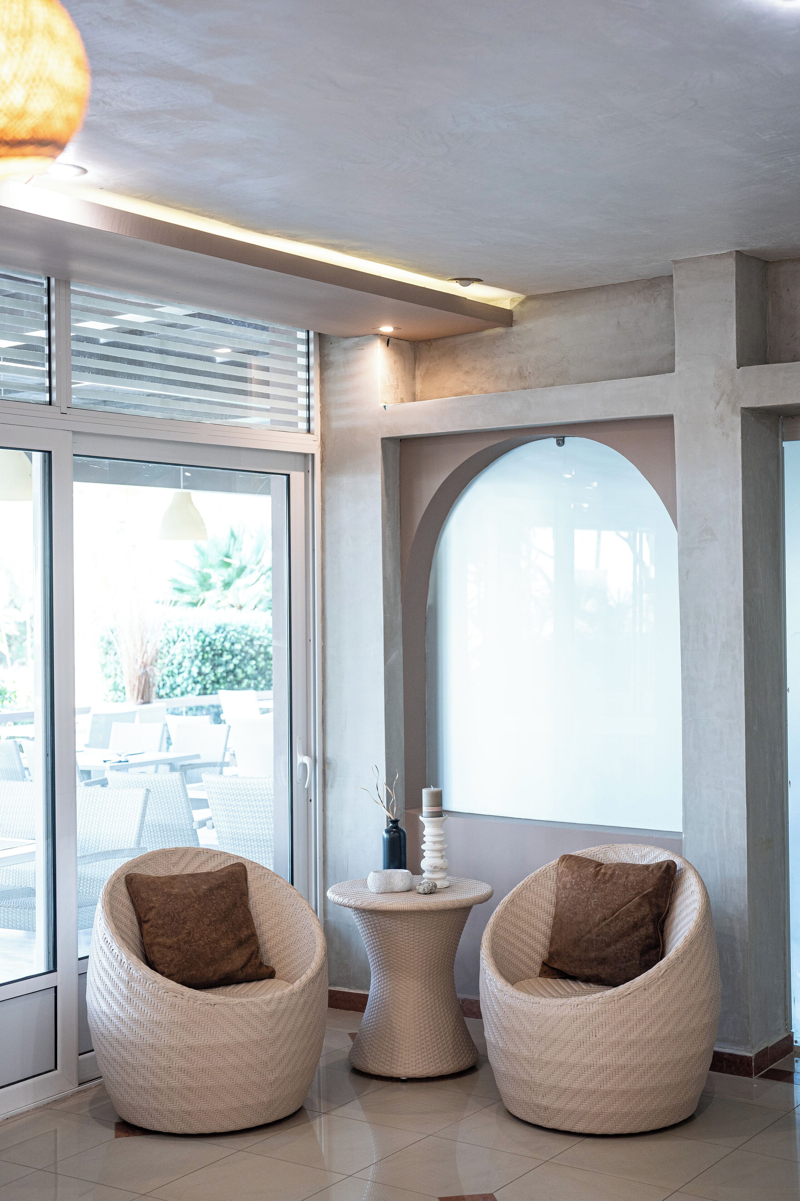 Un intérieur moderne avec deux fauteuils en osier, une petite table ronde et une grande fenêtre en arc de cercle.
