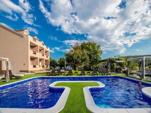 Relax by the unique pool with a central island, surrounded by lush greenery and comfortable lounge chairs.