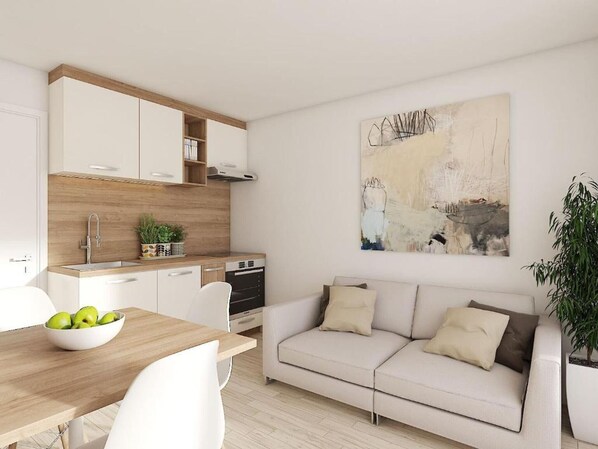 Une cuisine moderne avec des armoires blanches, un plan de travail en bois et un lave-vaisselle. On y trouve une table à manger avec un saladier de fruits et des chaises blanches. Un canapé beige se trouve dans l’espace salon, et un grand tableau abstrait orne le mur.