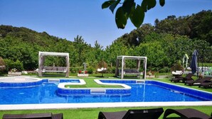 Une piscine au design géométrique, entourée de gazon synthétique et ombragée par des pergolas.