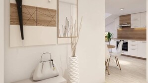 Un intérieur moderne avec un mur blanc, une œuvre d’art géométrique en bois, un parapluie noir, un sac à main blanc et un vase blanc orné de branches.