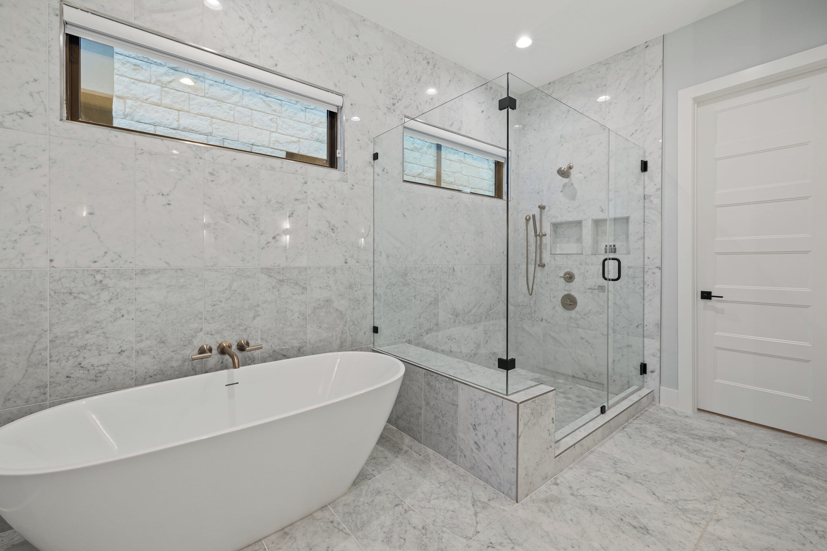 Un baño moderno con una bañera independiente, ducha con mampara de vidrio y una puerta blanca.