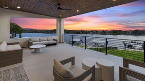 A modern outdoor deck with seating, a view of a lake, and a sunset.