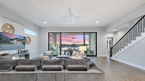 A spacious living room with a large gray sectional sofa, a ceiling fan, and a view through glass doors to the outside.
