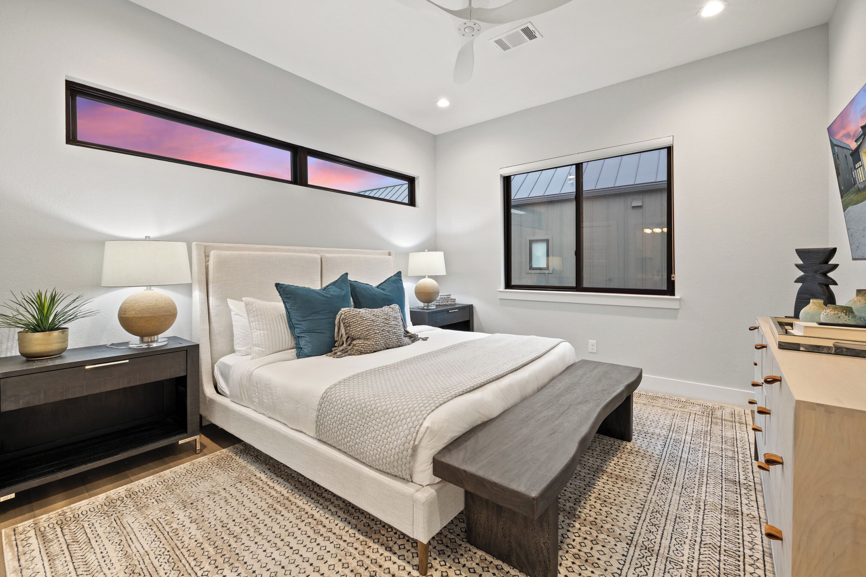 A bedroom with a bed, bedside tables, a nightstand, a window, and a ceiling fan.