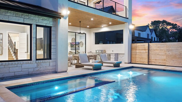 A modern pool area with a two-story building, outdoor seating, and a view of the sunset.