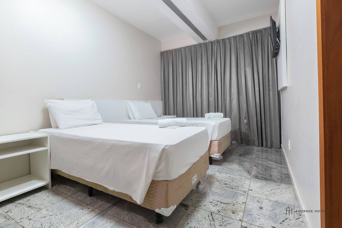 A hotel room with two single beds, a TV mounted on the wall, and a bathroom with a shower curtain.