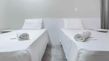 A hotel room with two single beds, each with a rolled white towel. The room has white bedding and a marble floor.