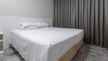 A modern hotel room with a large bed, a wooden headboard, and a grey curtain.