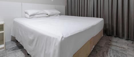 Une chambre d’hôtel moderne avec un grand lit, une tête de lit en bois et un rideau gris.