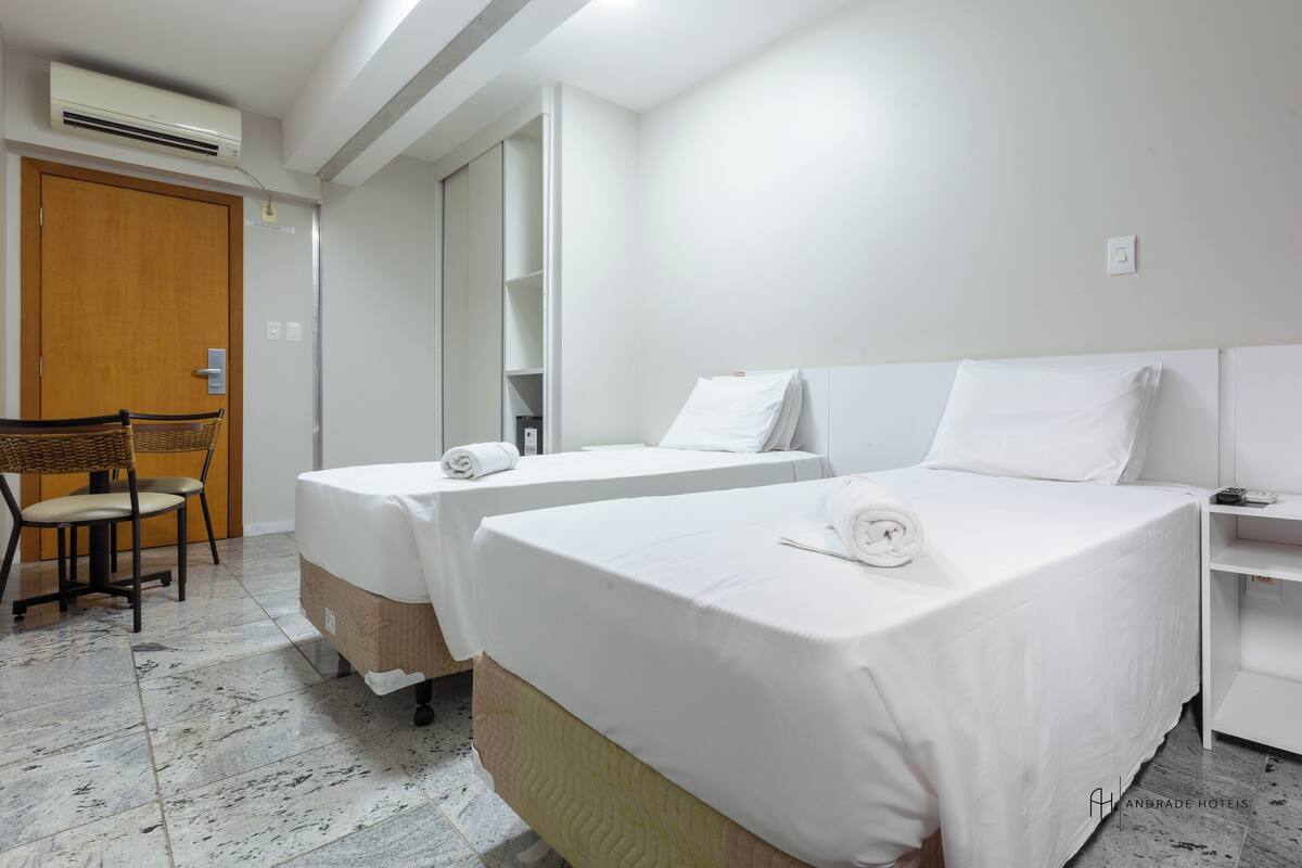 A hotel room with two single beds, a wooden door, a chair, and a white wardrobe.