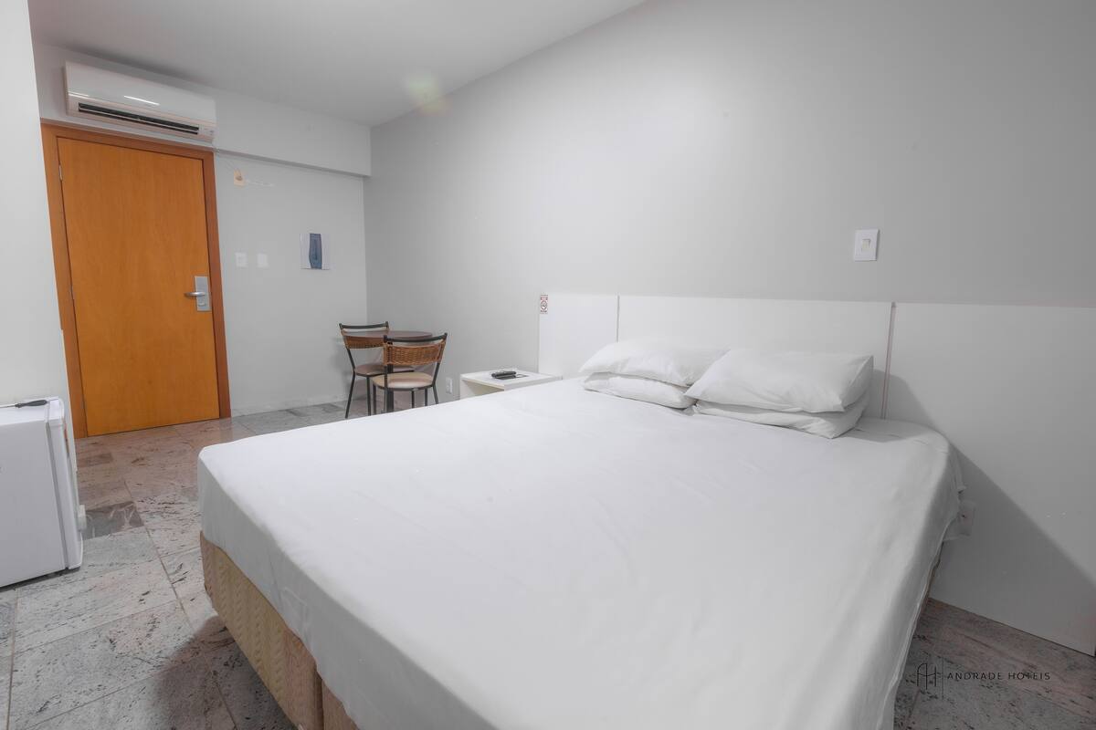 A hotel room with a bed, a chair, a small table, and a door.