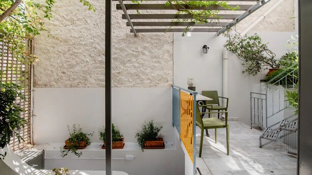 A sunlit patio with a pergola, green chairs, potted plants, and a small table. - Canto-Home Alongside The Acropolis (Athina)