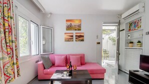A modern living room with a pink sofa, a coffee table with two wine glasses and a bottle, and a TV on a stand. - Canto-Home Alongside The Acropolis (Athina)