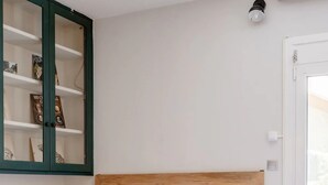 A bedroom with a wooden headboard, white bedding, a bedside table with a lamp, and a green-framed cabinet with books. - Canto-Home Alongside The Acropolis (Athina)
