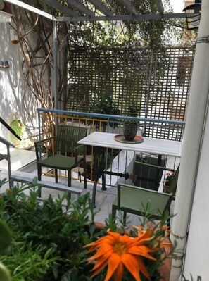 Une petite terrasse extérieure avec une table et deux chaises, entourée d’une clôture en bois et de plantes en pot.