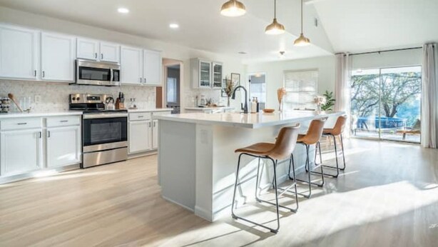 A modern kitchen with white cabinetry, stainless steel appliances, and a central island with bar stools.