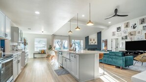 A modern kitchen with a central island, pendant lighting, and a dining area with a teal sofa.