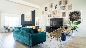 A spacious living room with a teal sofa, a television, and artwork on the walls.