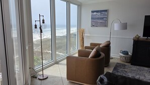Een woonkamer met grote ramen, een plafondventilator, een vloerlamp, een televisie en een open haard.