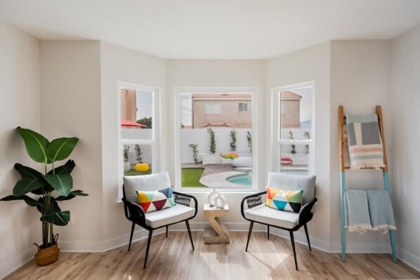 Ein Zimmer mit zwei Sesseln, die zu einem großen Fenster zeigen, einem kleinen Tisch, einer Pflanze und einer Holzleiter.