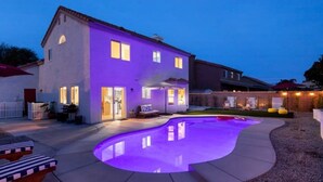 A house with a swimming pool, a patio, and a well-lit exterior.
